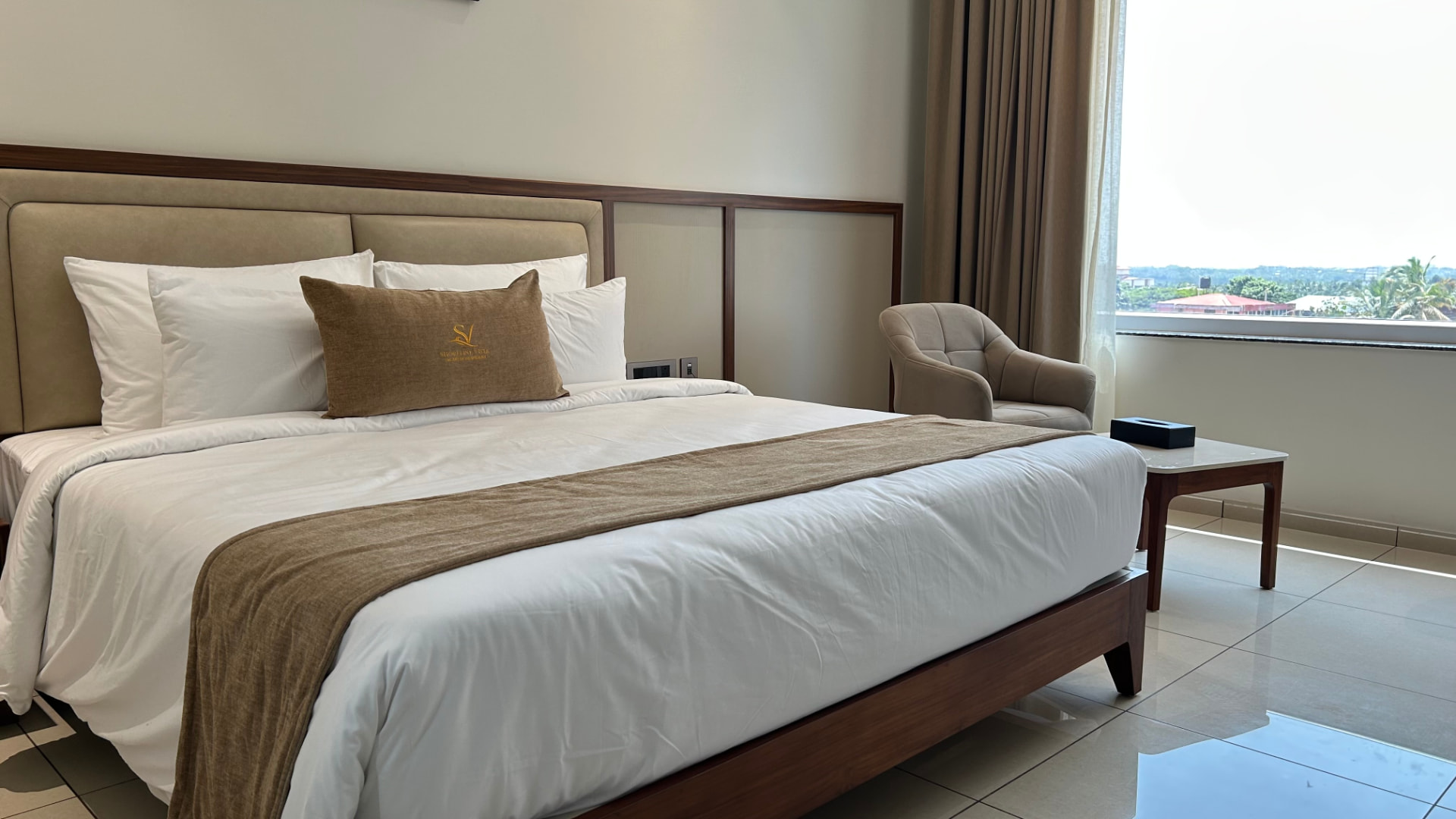 The Premium Room bed beside the window, with an armchair and side table